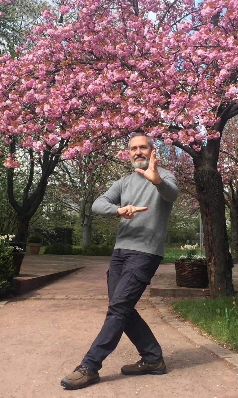 Michael Goddard in a practice posture beneath a blossoming cherry tree
